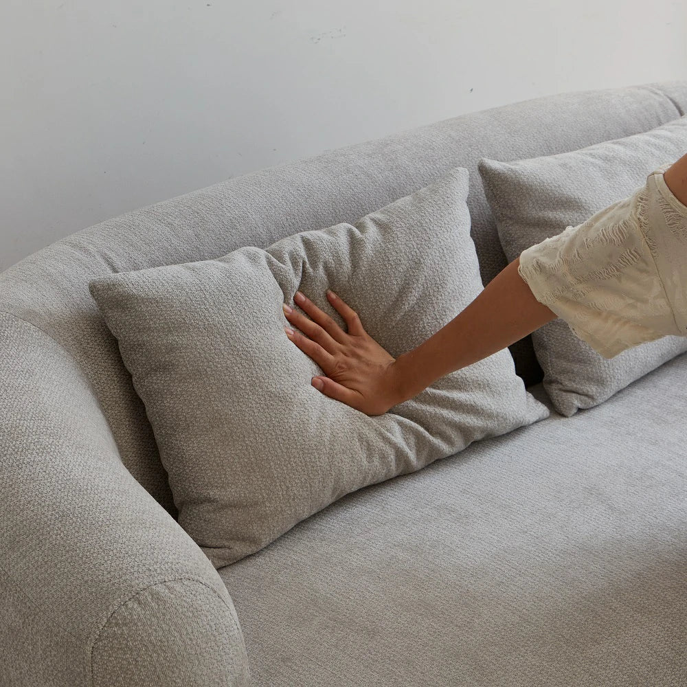 Hand pressing soft back pillow of grey 2-seater couch